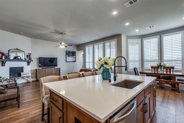 kitchen featuring sink, stainless steel dishwasher, dark hardwood / wood-style floors, a fireplace, and an island with sink