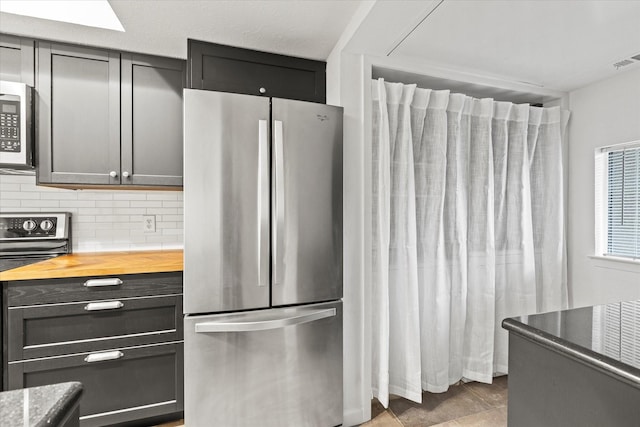 kitchen featuring appliances with stainless steel finishes, butcher block countertops, and tasteful backsplash