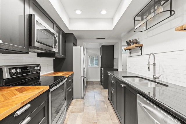 kitchen featuring sink, decorative backsplash, a tray ceiling, butcher block countertops, and stainless steel appliances