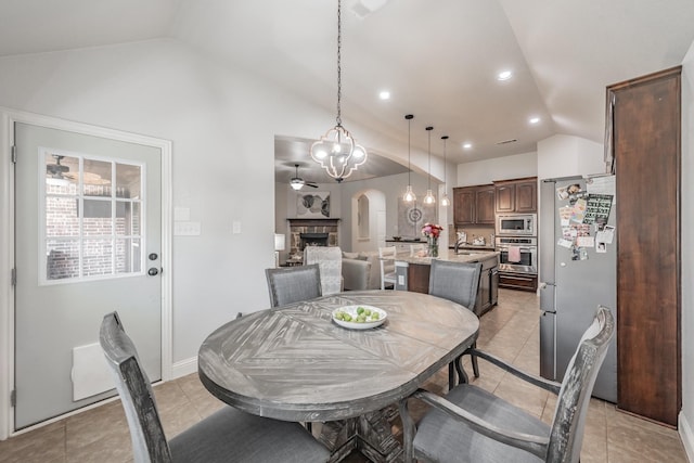 tiled dining area with a fireplace, vaulted ceiling, sink, and ceiling fan