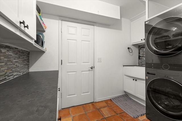 laundry area with stacked washer and dryer, tile patterned flooring, and cabinets