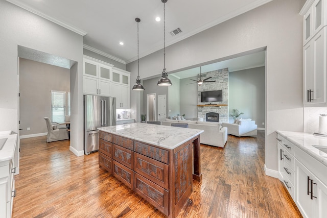 kitchen with white cabinets, stainless steel fridge, a kitchen island, and light stone countertops