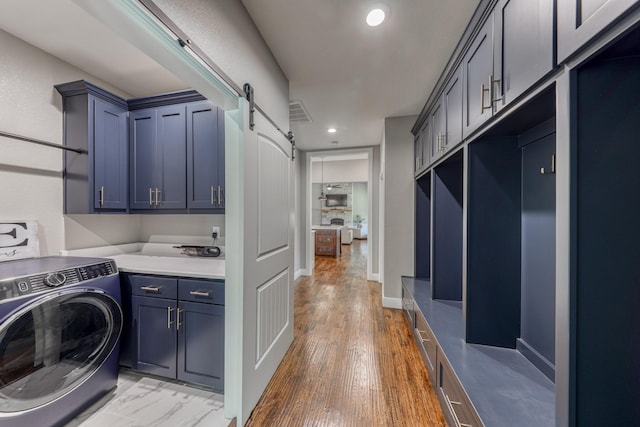 clothes washing area featuring cabinets, washer / dryer, a barn door, and hardwood / wood-style flooring