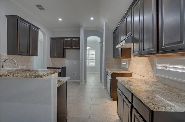 kitchen with tasteful backsplash, light stone countertops, light tile patterned flooring, crown molding, and sink