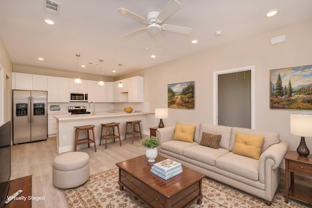 living room featuring ceiling fan, sink, and light hardwood / wood-style flooring