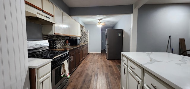 kitchen with backsplash, hardwood / wood-style flooring, ceiling fan, light stone countertops, and appliances with stainless steel finishes