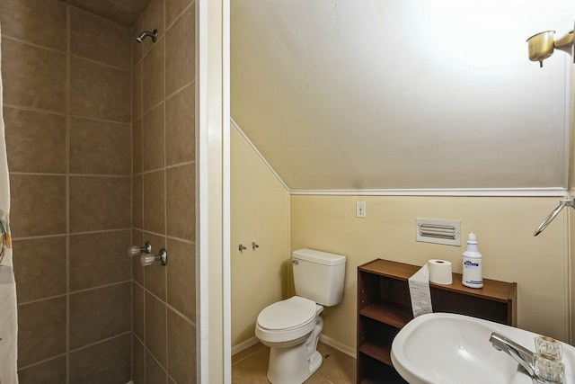 bathroom with sink, tile patterned flooring, a tile shower, vaulted ceiling, and toilet