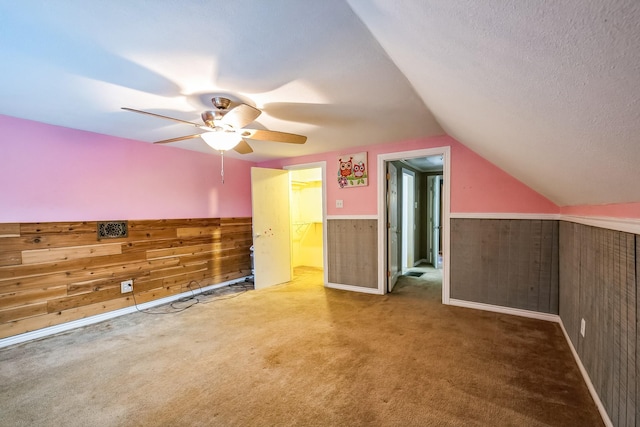 additional living space with vaulted ceiling, a textured ceiling, wooden walls, ceiling fan, and carpet