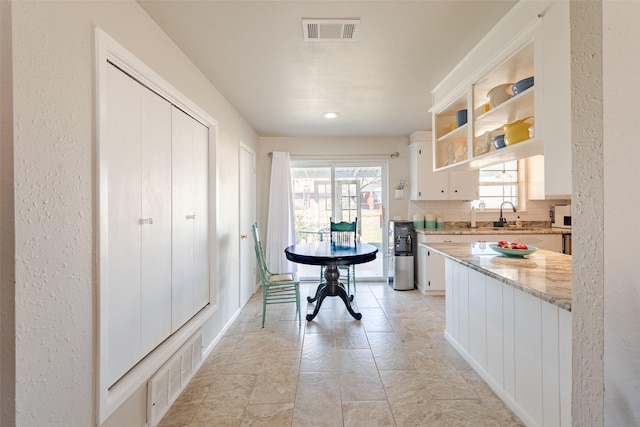 kitchen with light stone countertops, backsplash, white cabinetry, and sink