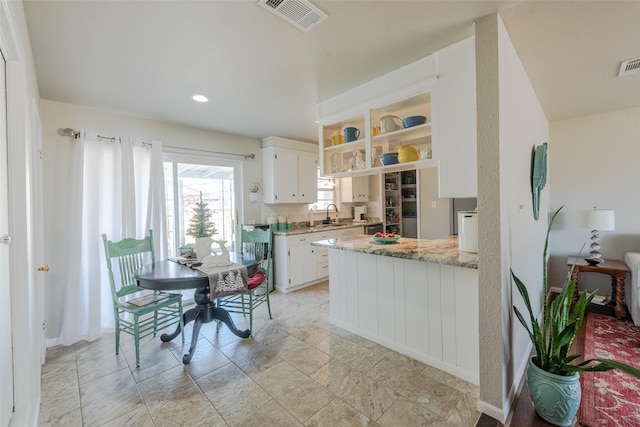 kitchen with sink, tasteful backsplash, light stone counters, kitchen peninsula, and white cabinets