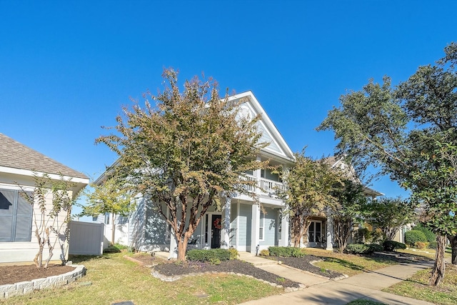 view of property hidden behind natural elements with a balcony and a front lawn