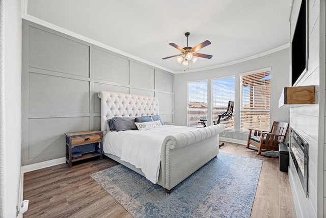 bedroom with light wood-type flooring, ornamental molding, a ceiling fan, and a decorative wall