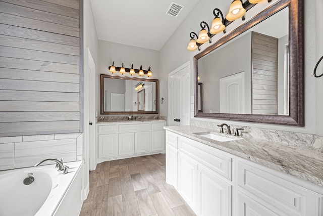 full bath featuring a sink, visible vents, two vanities, and a bath