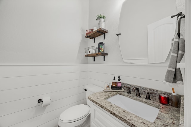 bathroom with wooden walls, toilet, and vanity