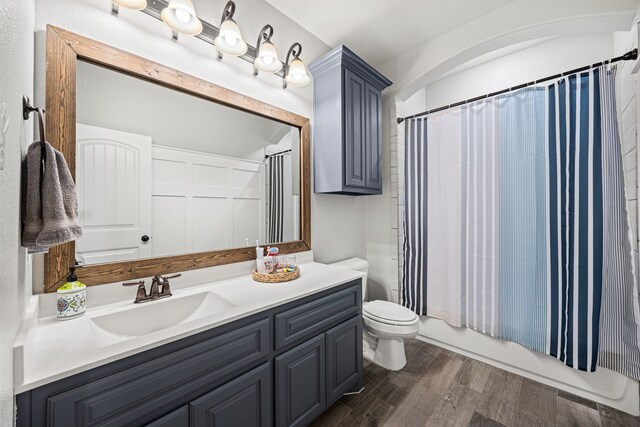 bathroom with toilet, wood finished floors, vanity, and shower / bath combination with curtain