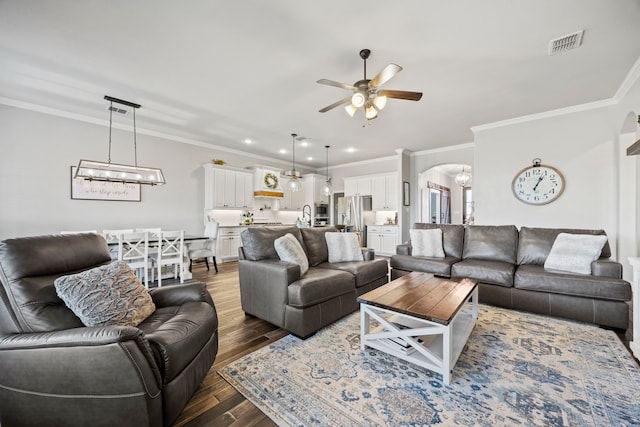 living room featuring visible vents, ornamental molding, ceiling fan with notable chandelier, wood finished floors, and arched walkways