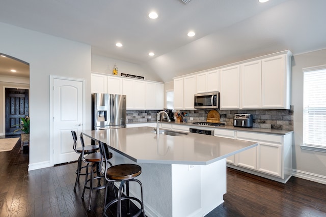 kitchen with sink, dark hardwood / wood-style floors, an island with sink, vaulted ceiling, and appliances with stainless steel finishes