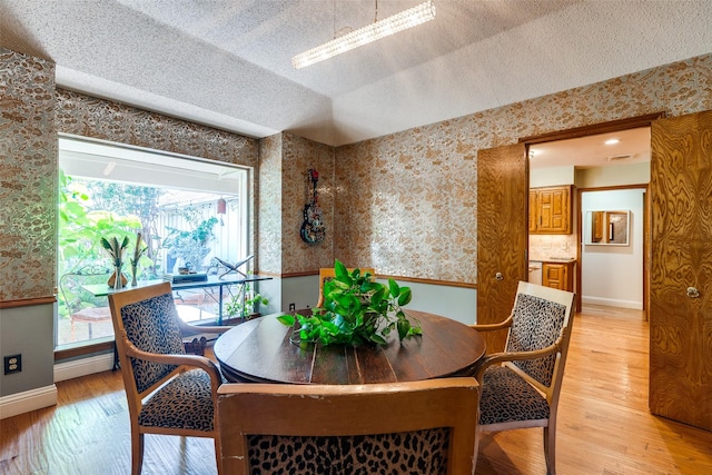 dining space with vaulted ceiling, a textured ceiling, and light wood-type flooring