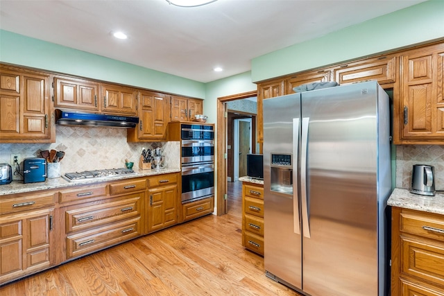 kitchen with appliances with stainless steel finishes, light stone countertops, light hardwood / wood-style flooring, and backsplash