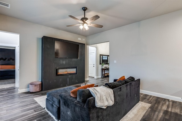 living room featuring ceiling fan, a large fireplace, and dark wood-type flooring