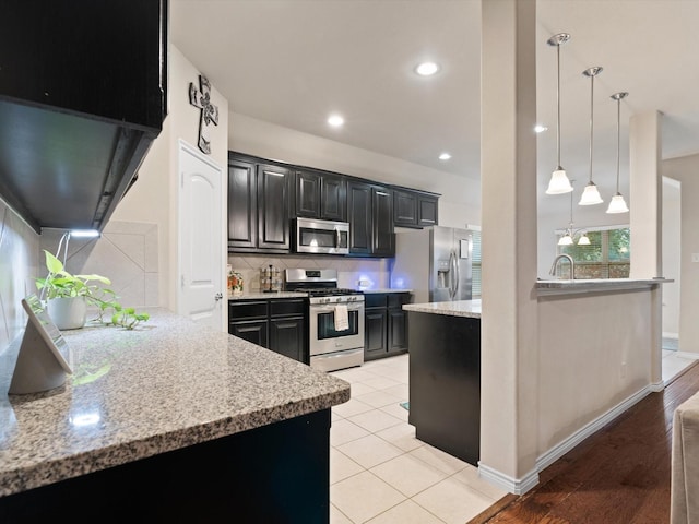 kitchen with light stone countertops, sink, hanging light fixtures, stainless steel appliances, and tasteful backsplash