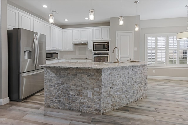 kitchen featuring stainless steel appliances, light stone countertops, sink, and a kitchen island with sink