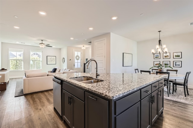 kitchen with sink, dark wood-type flooring, dishwasher, light stone countertops, and an island with sink