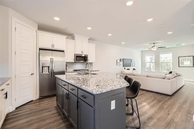 kitchen featuring sink, dark wood-type flooring, stainless steel appliances, a center island with sink, and white cabinets