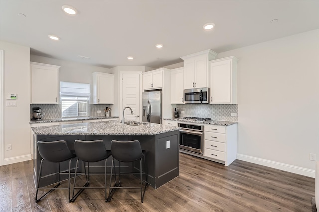 kitchen with appliances with stainless steel finishes, dark hardwood / wood-style flooring, a breakfast bar, a kitchen island with sink, and white cabinets