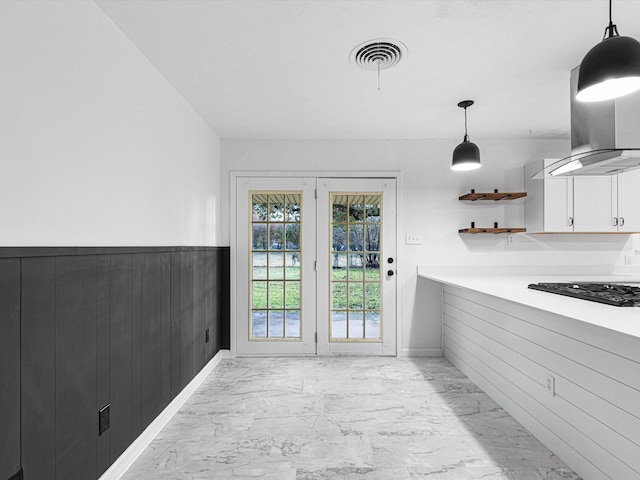 kitchen featuring black gas stovetop, ventilation hood, wooden walls, pendant lighting, and white cabinetry