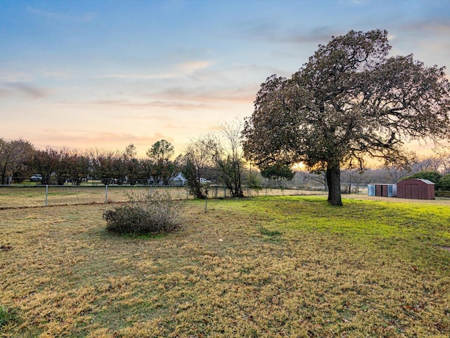 yard at dusk with a rural view and a storage unit