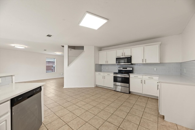 kitchen featuring tasteful backsplash, white cabinets, stainless steel appliances, and light tile patterned floors