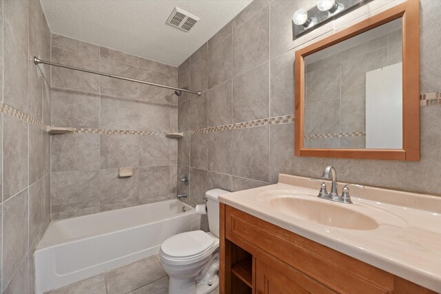 full bathroom featuring vanity, tiled shower / bath combo, toilet, a textured ceiling, and tile walls