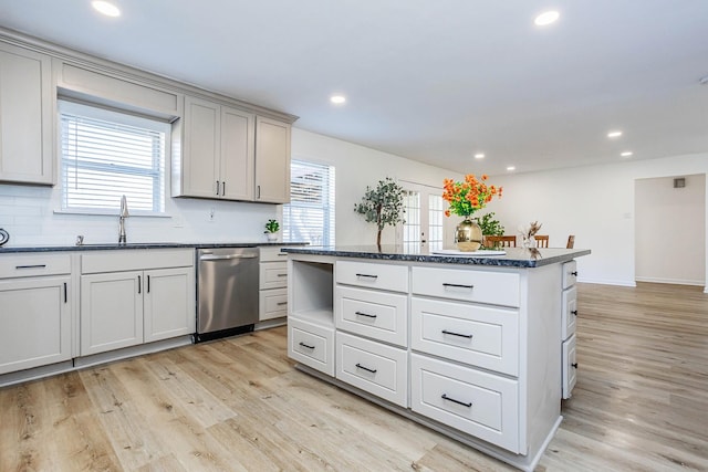 kitchen featuring backsplash, stainless steel dishwasher, sink, light hardwood / wood-style floors, and a kitchen island