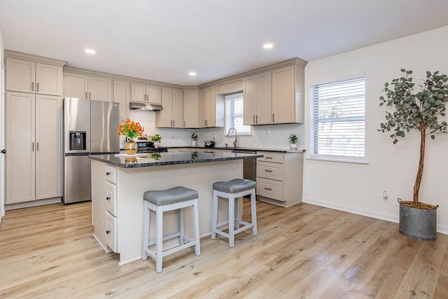 kitchen featuring appliances with stainless steel finishes, sink, light hardwood / wood-style flooring, dark stone countertops, and a center island