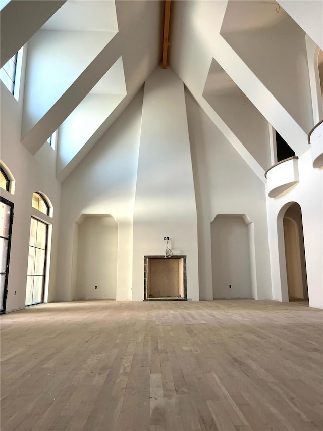 unfurnished living room featuring beam ceiling, wood finished floors, arched walkways, and a towering ceiling