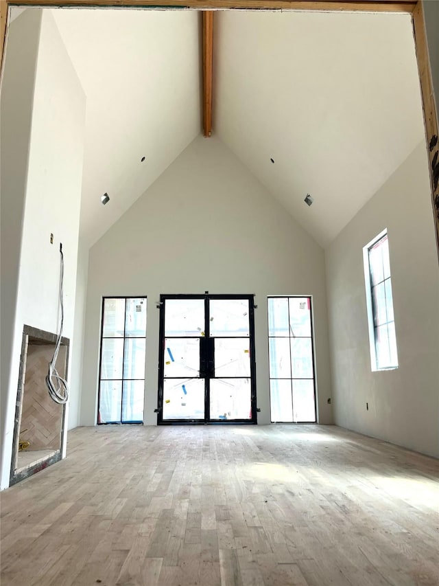 unfurnished room with light wood-type flooring, beam ceiling, and high vaulted ceiling