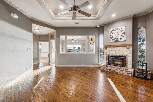 unfurnished living room with hardwood / wood-style flooring, a stone fireplace, a raised ceiling, and crown molding