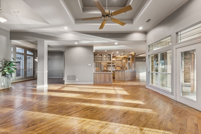 unfurnished living room with decorative columns, a raised ceiling, ceiling fan, crown molding, and hardwood / wood-style floors