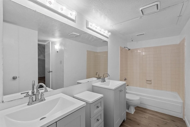 full bathroom featuring tiled shower / bath combo, hardwood / wood-style floors, a textured ceiling, toilet, and vanity