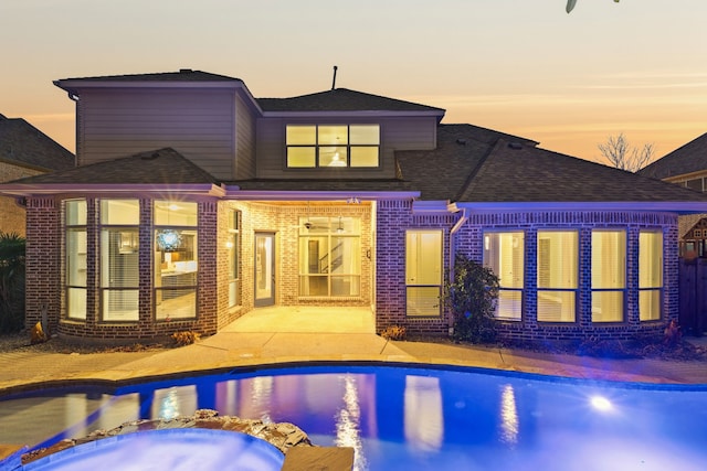 pool at dusk featuring a patio and an in ground hot tub