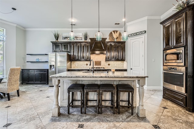 kitchen featuring light stone countertops, dark brown cabinetry, stainless steel appliances, pendant lighting, and an island with sink