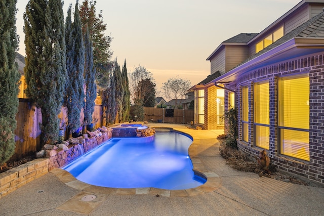 pool at dusk featuring an in ground hot tub and a patio area