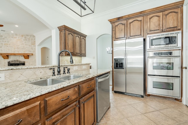 kitchen featuring light stone countertops, stainless steel appliances, crown molding, sink, and a stone fireplace