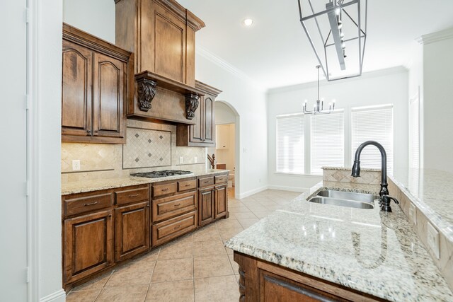 kitchen featuring pendant lighting, light stone counters, stainless steel gas cooktop, and sink