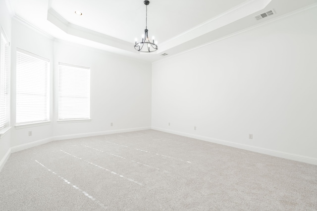 carpeted empty room featuring a chandelier, a raised ceiling, and ornamental molding