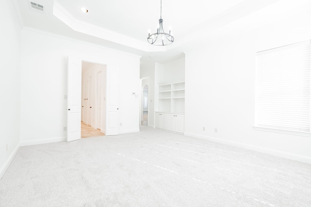 carpeted spare room featuring an inviting chandelier, a raised ceiling, and crown molding