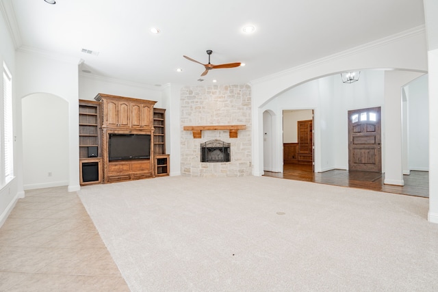 unfurnished living room with light tile patterned floors, a stone fireplace, ceiling fan, and crown molding