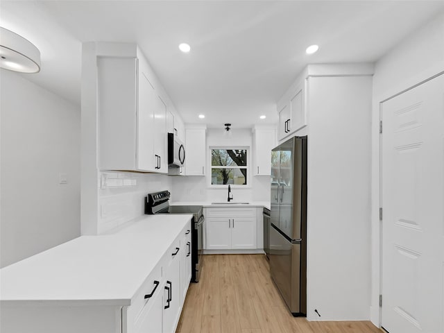 kitchen with white cabinetry, sink, backsplash, stainless steel appliances, and light hardwood / wood-style flooring