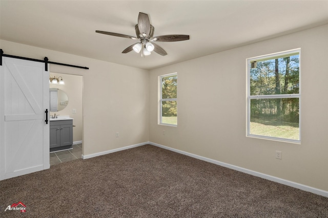 unfurnished bedroom featuring carpet flooring, ensuite bath, ceiling fan, sink, and a barn door